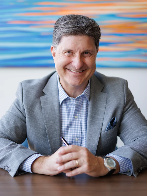 Lewis Gelmon seated at a desk, smiling in a professional setting, representing his role as Managing Partner at Acuity Negotiations.